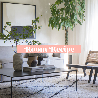 Japandi living room with beige sofa, coffee table, wooden chair and floor lamp to the left, plant and picture on wall to the right, berber rug on floor