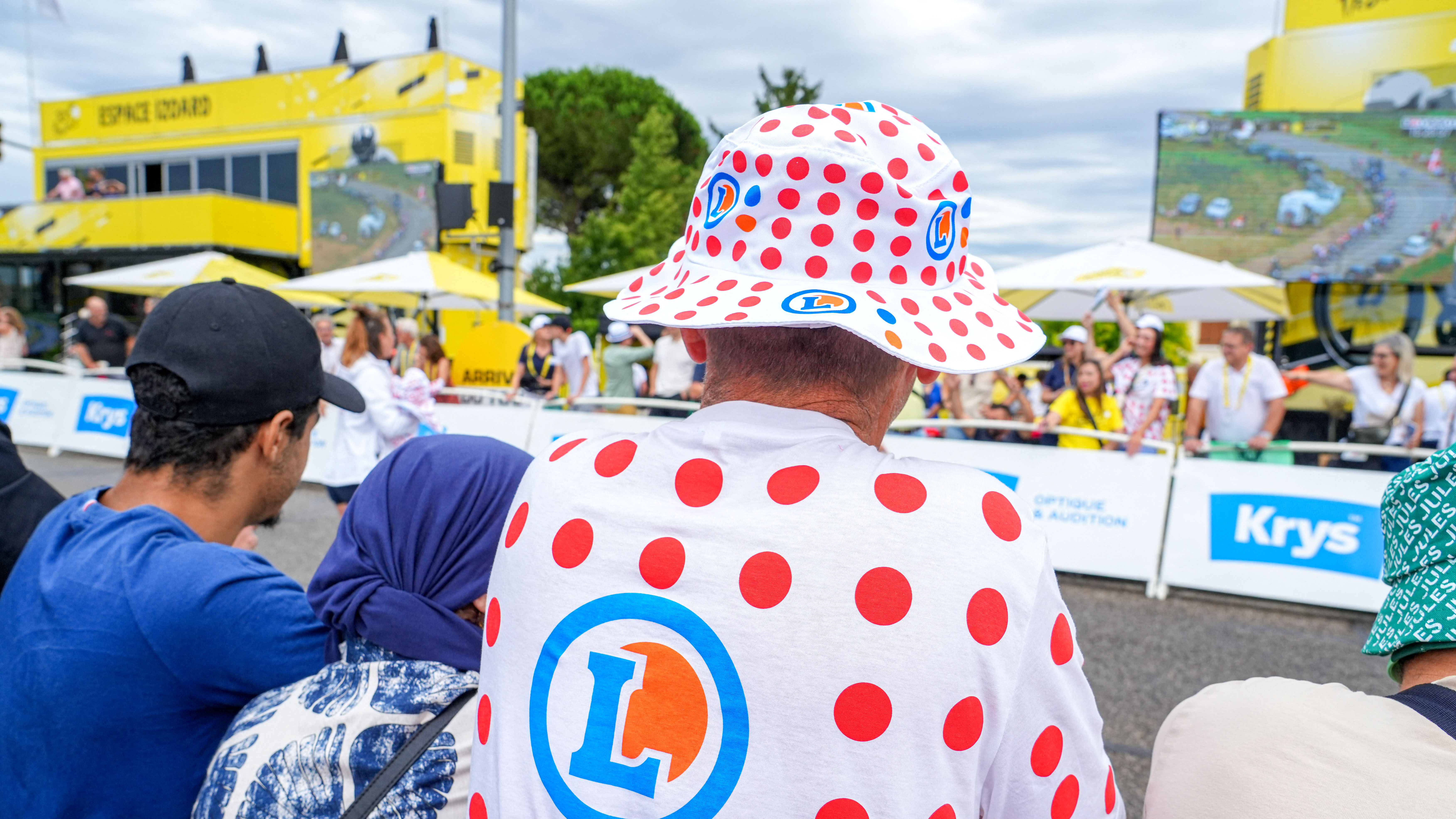 A man wearing a T-shirt and a white bob with red polka dots from the Leclerc supermarket is thrown by hostesses along the barriers around the finish line of the 17th stage of the men s Tour de France cycling race, in Valence, France, on July 23, 2025. On the lookout for goodies and gifts from the publicity caravan.
