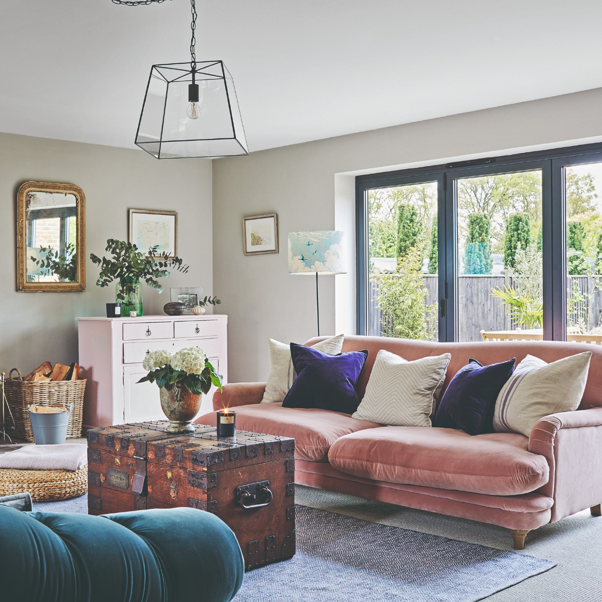 A grey living room with large windows and a pink velvet sofa