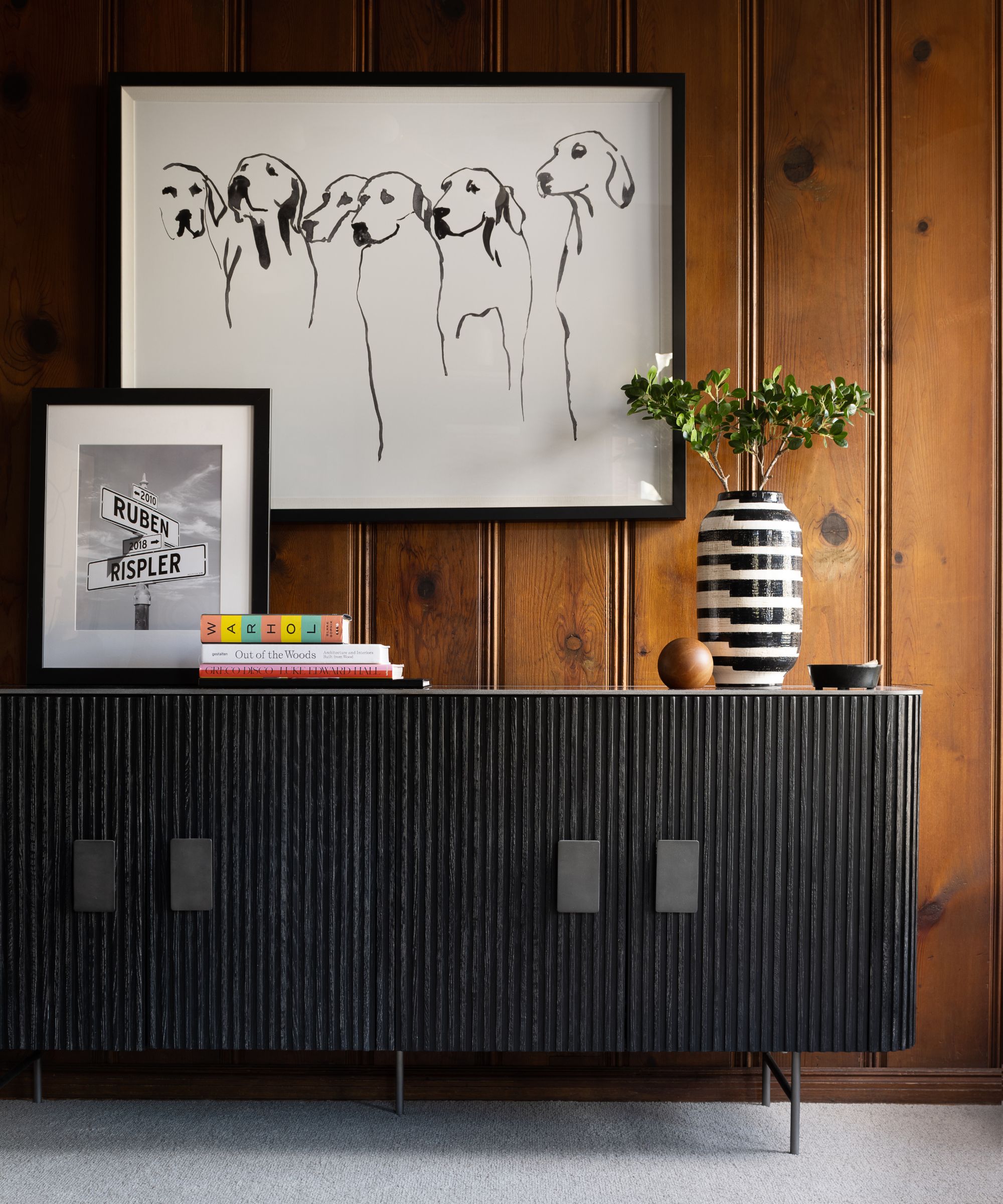 Wooden paneled wall with black fluted sideboard and line artwork on the wall of six dogs