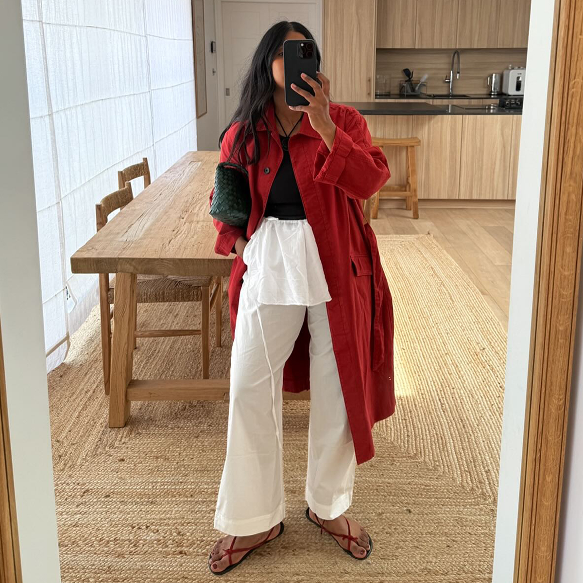@monikh wears a red trench coat with white linen trousers