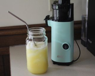 A freshly prepared apple-pineapple juice in a glass jam jar with metal straw using the Dash Compact Power juicer small kitchen appliance
