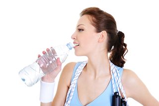A woman stands with a jump rope, drinking water