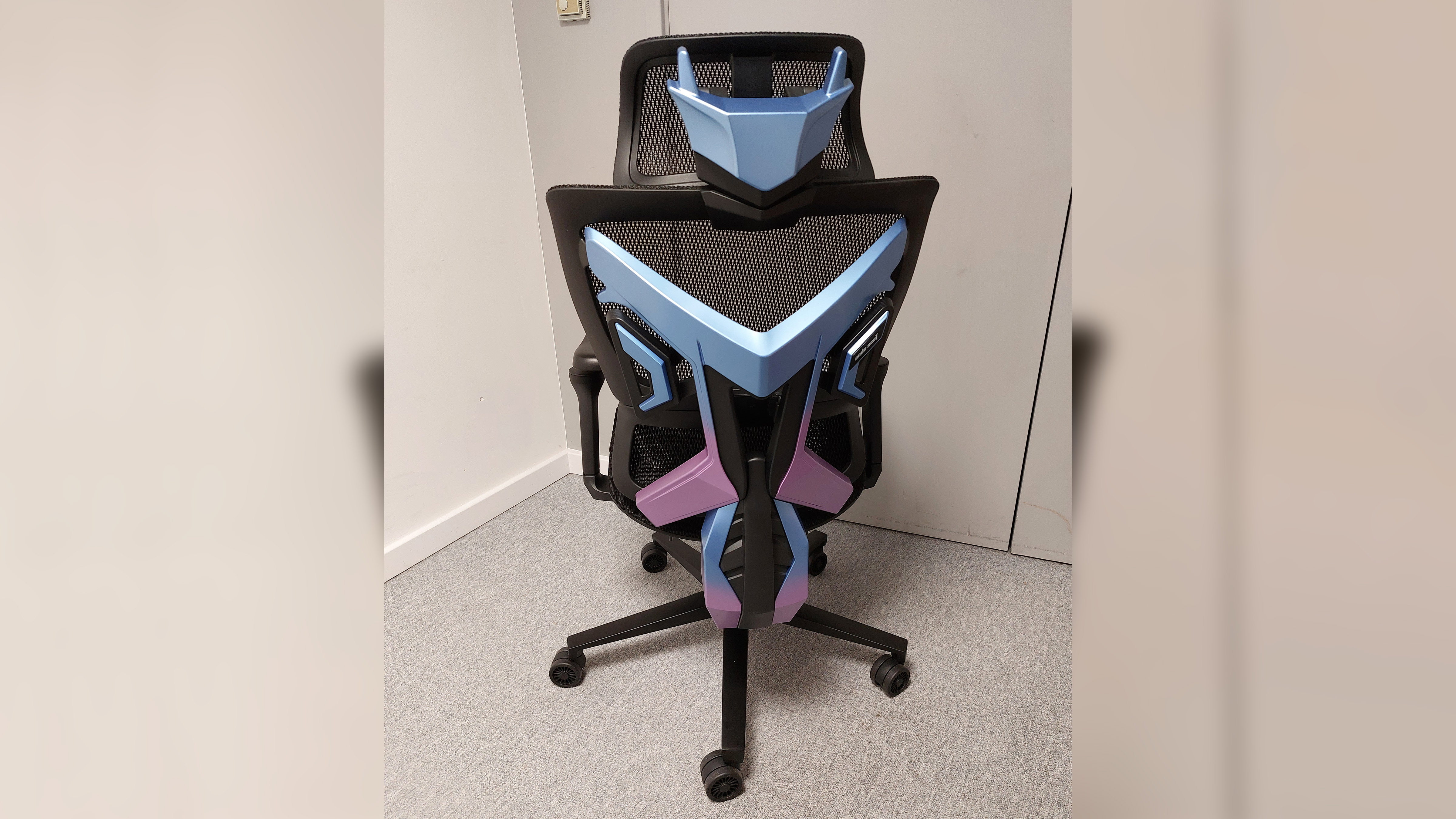 A full back view of the AndaSeat X-Air Pro Mesh Office Gaming Chair. The plastic back frame comes in two seperate parts, the 'head' and the 'spine'. It is thick, robust, blue and purple plastic attached to the back frame of an otherwise ordinary office chair.