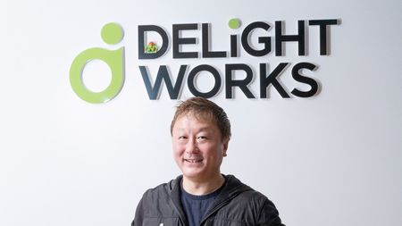 Yoshinori Ono in front of a DelightWorks logo, with his Blanka figure perched in the "D"