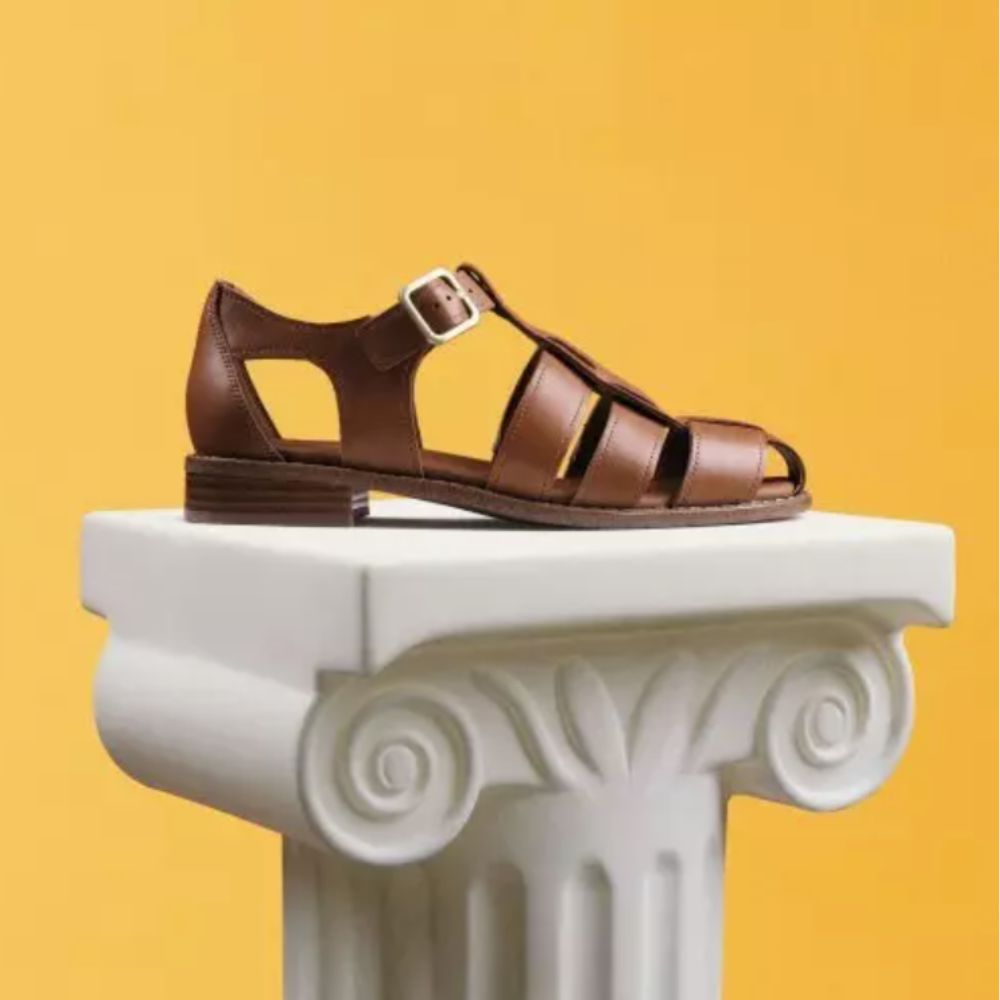 Clarks brown leather gladiator sandal on white Olympic pillar, with yellow background