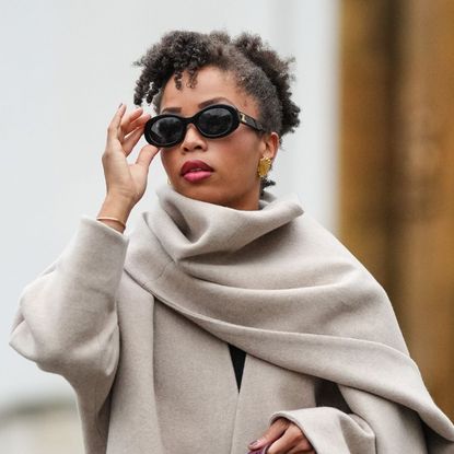 woman with coily hair wearing sunglasses and a beige coat and scarf - best shampoo for curly hair