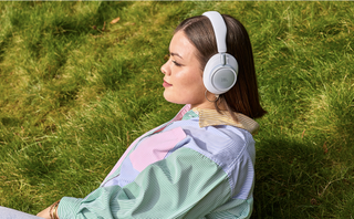 A woman sitting on grass wearing a white pair of JBL Live 780NC headphones