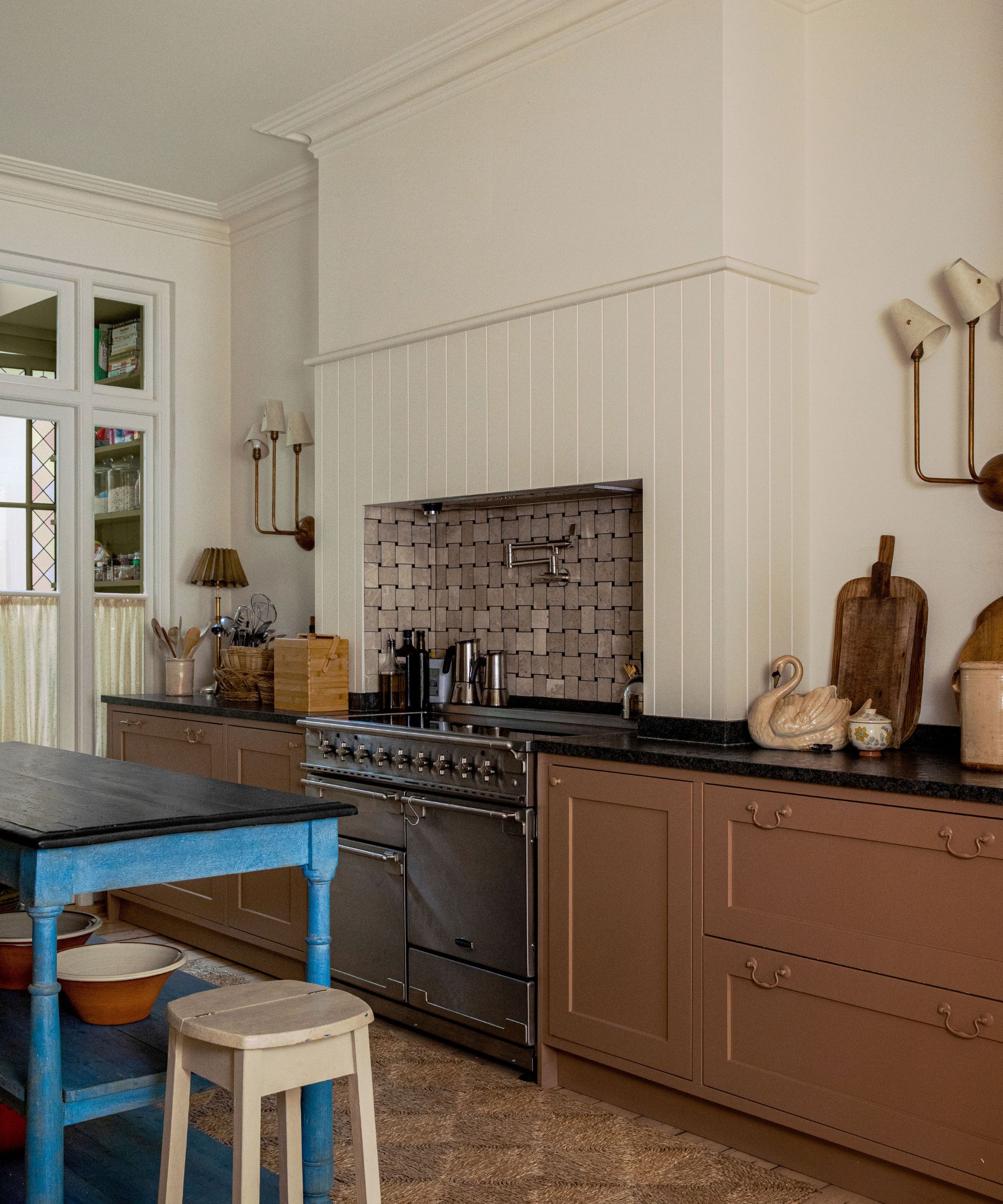 Farmhouse kitchen with cream walls, wood panelling, a tiled backsplash with a silver range cooker, mid-brown painted cabinetry, and a blue wooden freestanding island.