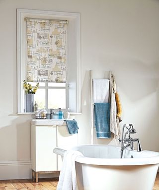 Breezy bathroom with freestanding roll top bath and charming patterned roller blind