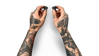 Tattooed hands holding a pair of Marshall Motif ANC earbuds