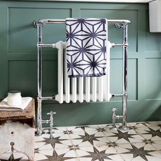 white and silver bathroom radiator against green panelling and on top of white and grey patterned tiles