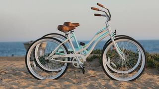 Two Retrospec e-bikes standing up on a sandy beach as the sun sets