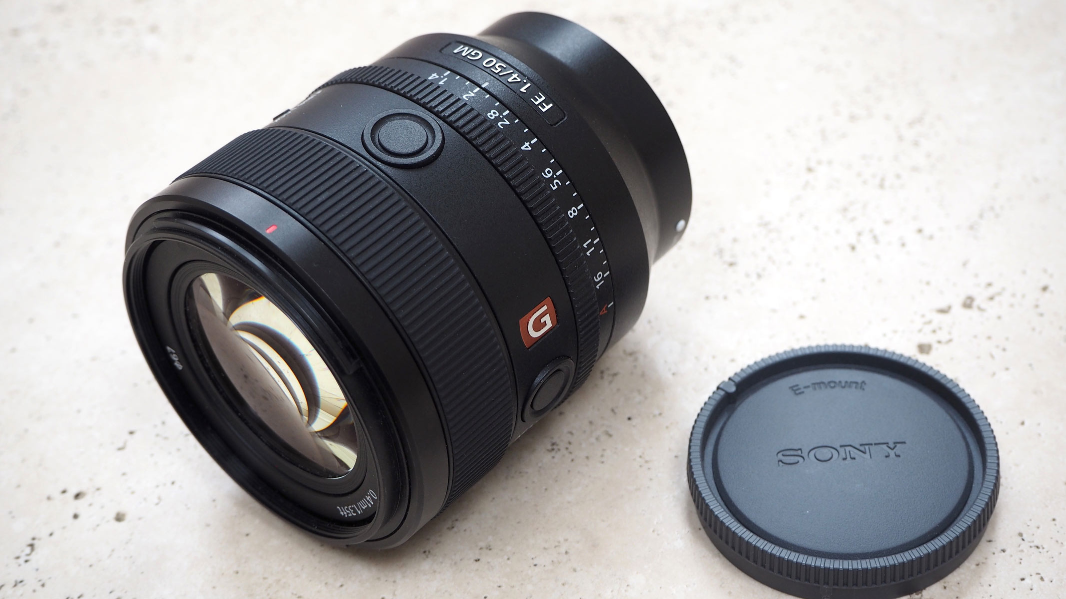The Sony 50mm f/1.4 GM lens and lens cap on a table.