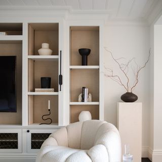 A white-painted living room in Lick's White 02 with built-in shelving, a display pedestal and a white boucle accent chair