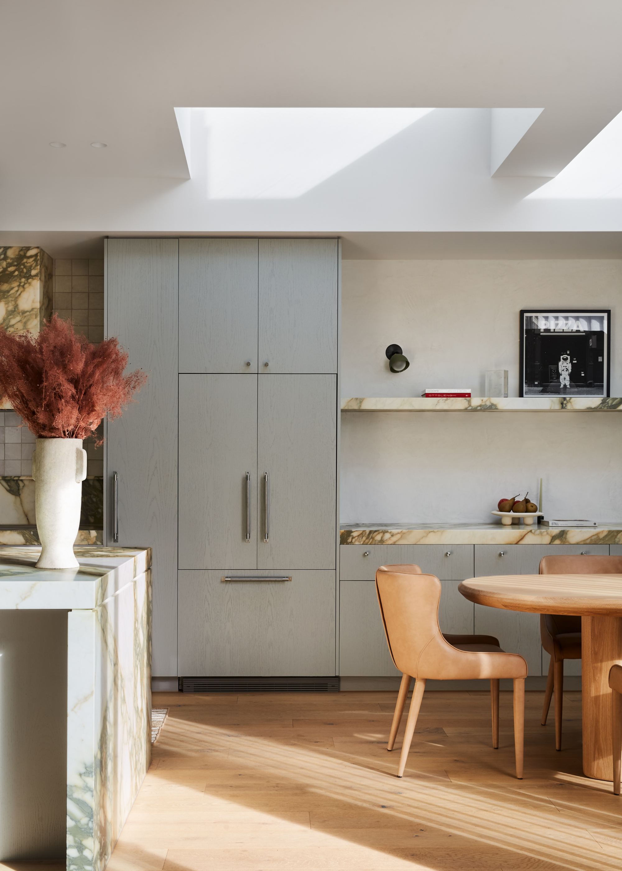 A minimalist blue-gray kitchen with floor to ceiling cabinetry, skylights, and a wood dining area to the right
