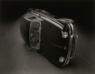 Black & white photograph of an old-school car turned on its side.