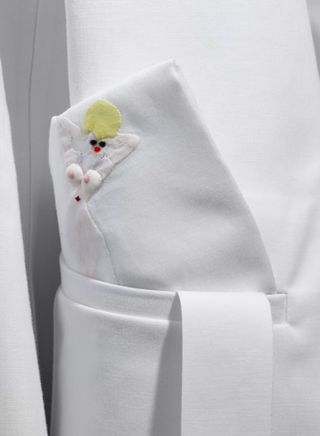 Close up view of a white coat by Carlo Brandelli featuring a hand embroidered handkerchief with a female figure on it that has blonde hair, red lips and her chest exposed at Matthew Brannon's show