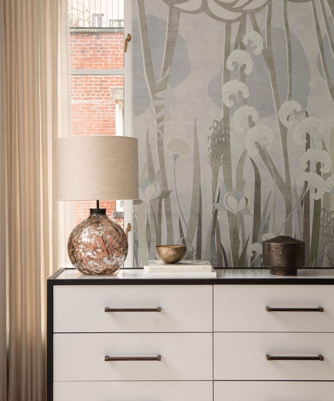 A white dresser with black details in front of a floral wallpapered wall