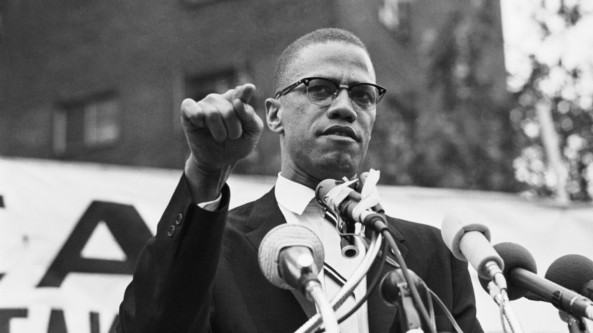 Black and white photograph of Malcolm X speaking into microphones