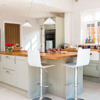 kitchen with white wall white cabinets wooden counter and white chairs