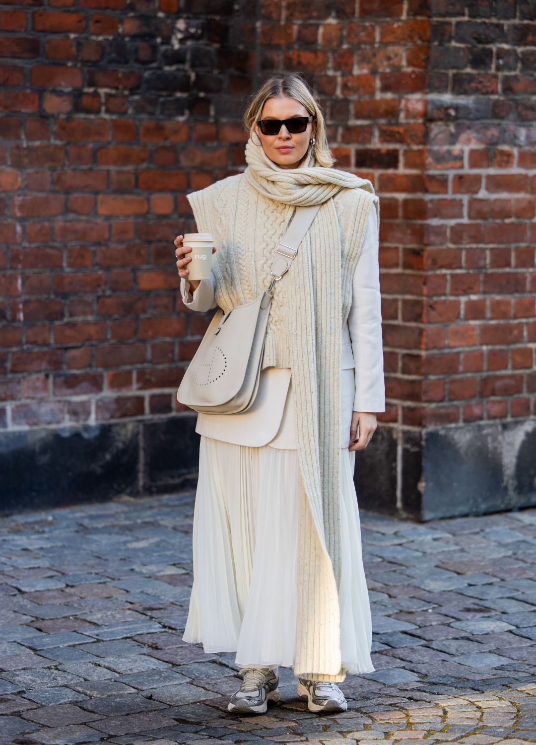 Hollie Mercedes Peters wears Loewe bag, creme white sleeveless knit, pleated skirt in beige, blazer, scarf outside Herskind during the Copenhagen Fashion Week AW24 on January 31, 2024 in Copenhagen, Denmark.