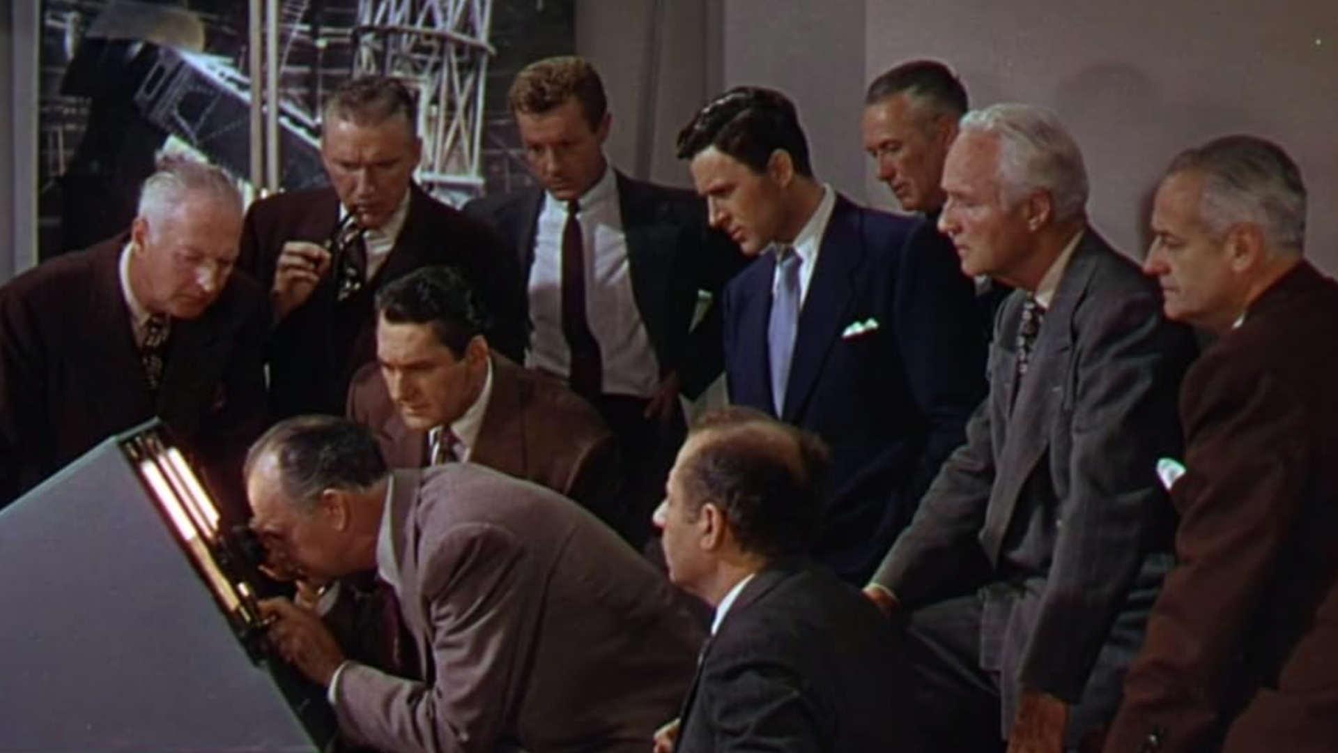 A group of men in suits are gathered around a computer and look concerned.