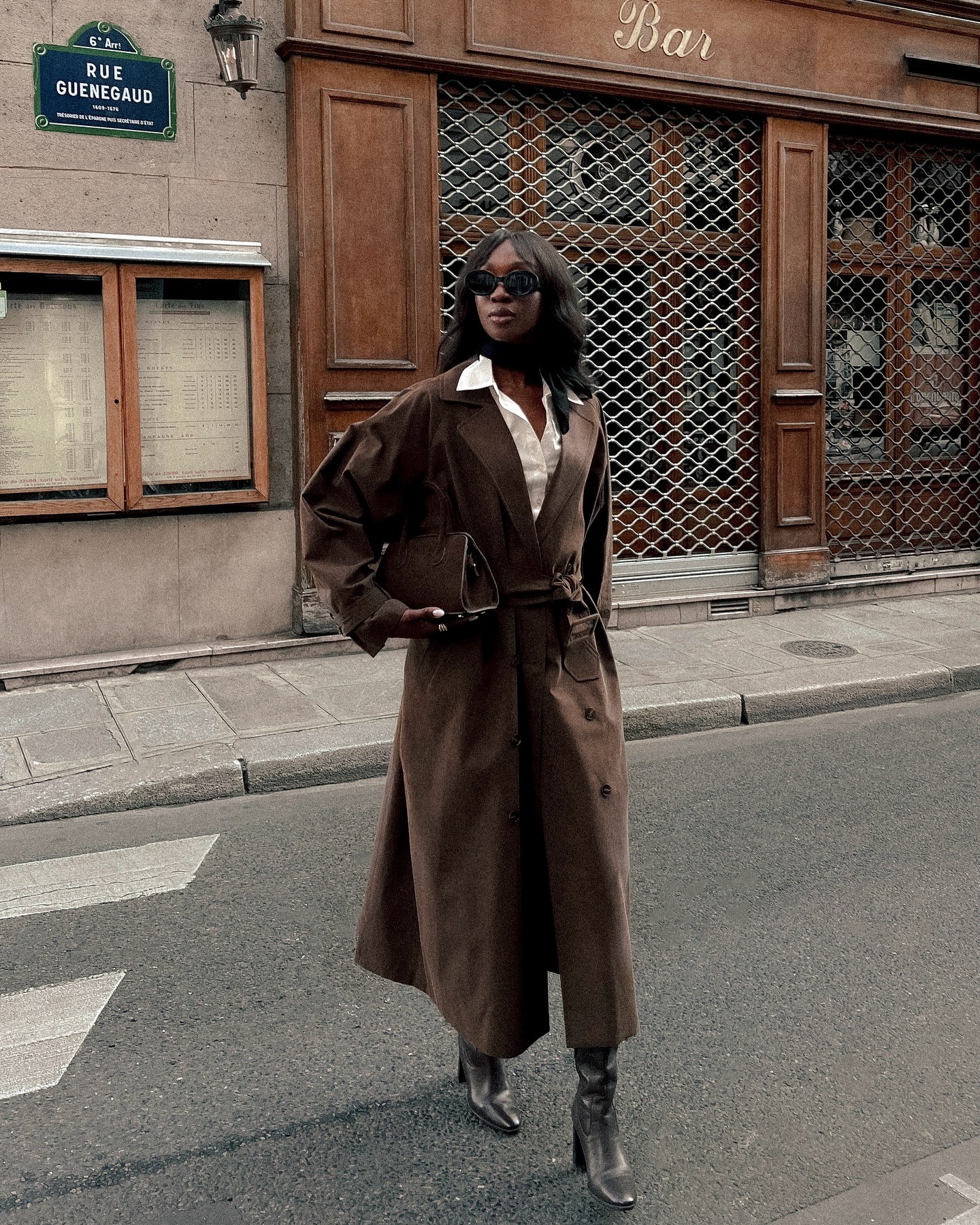 French influencer @emmanuellek_ wears a chocolate brown trench coat with brown knee-high boots.