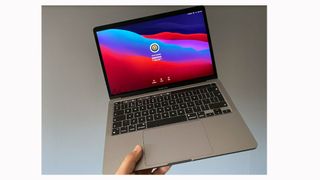 Image shows a hand holding out an open, turned on MacBook Pro 1.