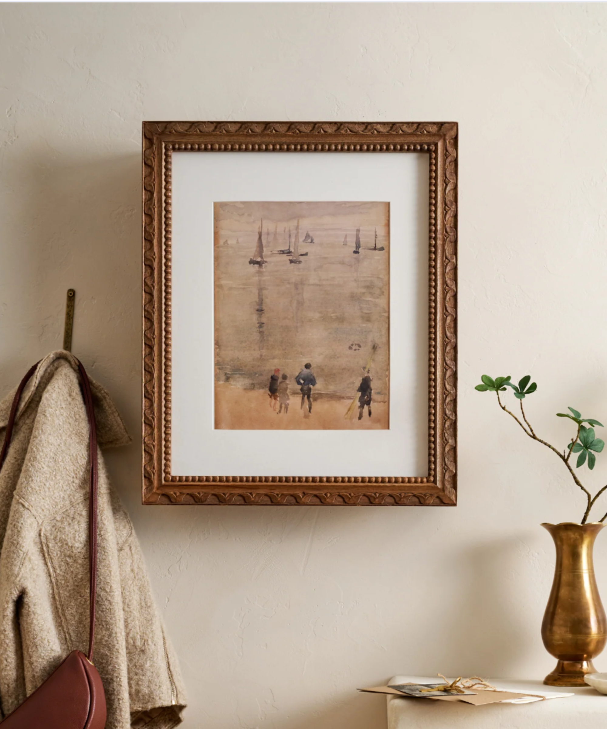 a picture frame in a scene with a hook holding up a jacket and a purse and a small table holding a vase with a branch inside