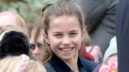 Princess Charlotte wearing a green plaid coat smiling at the camera amid a crowd of people