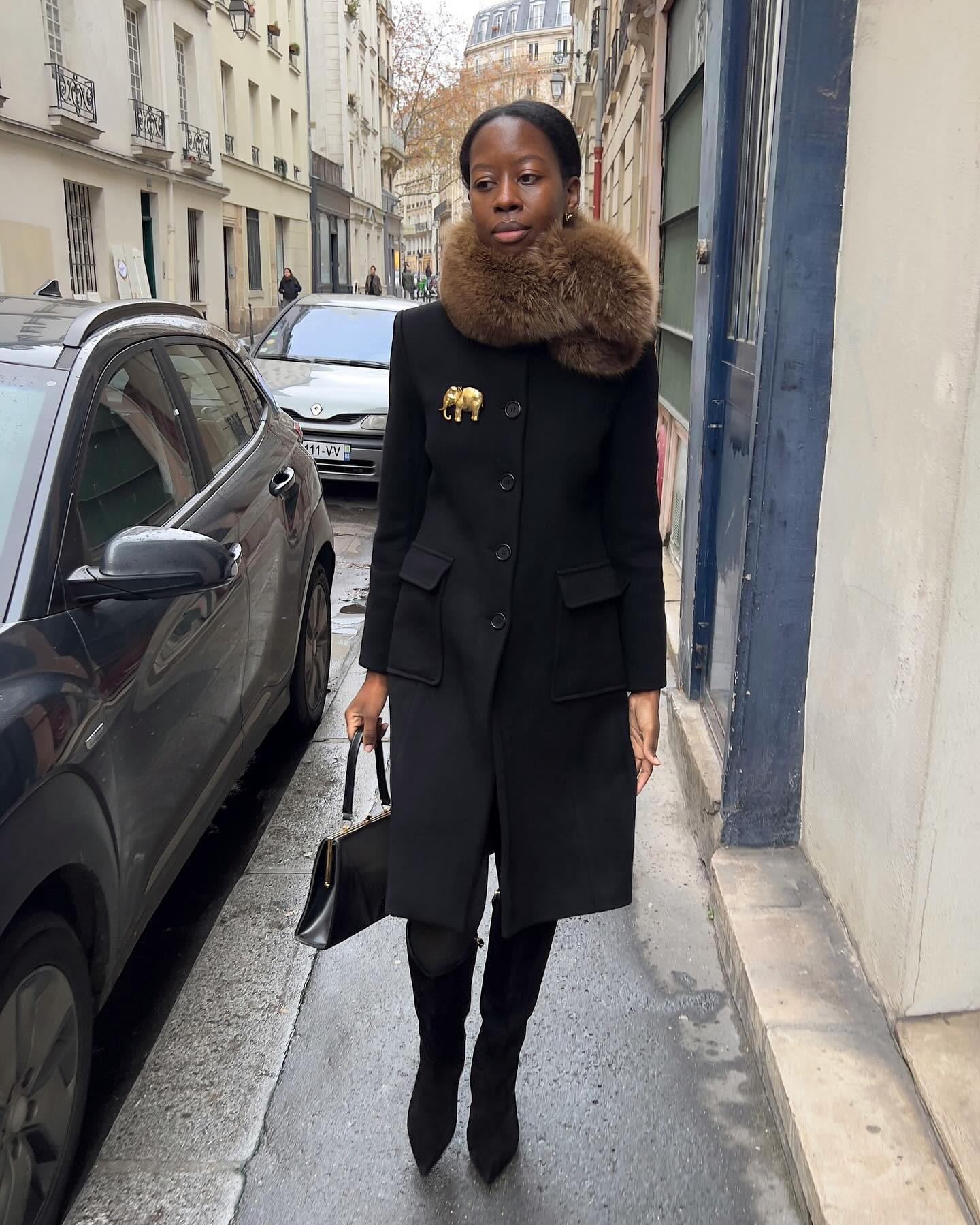 Parisian woman wears a faux fur stole, black coat and knee high black boots.