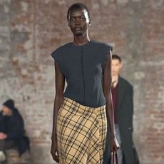 An Ami Paris model wearing a gray top, plaid skirt, and black leather boots