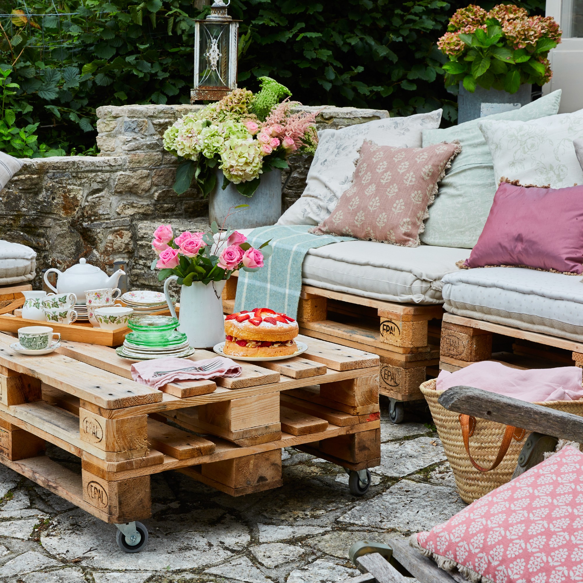 A garden with seating a coffee table built from pallets with seat and scatter cushions added on top