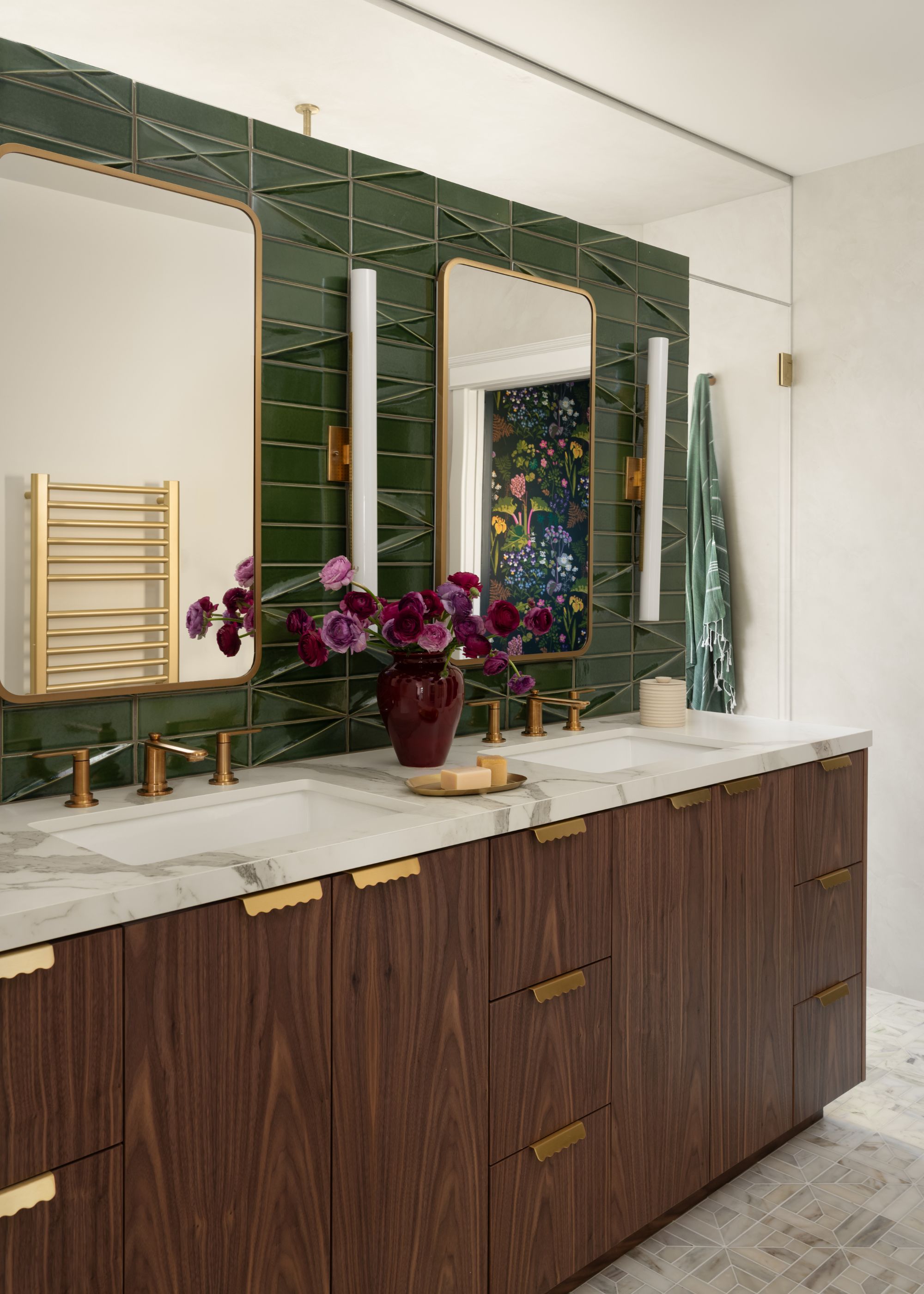 A dark wood bathroom vanity with double sunks on top as well as double mirrors on top of a green tiled wall