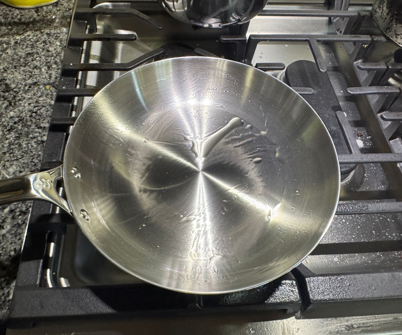 A small stainless steel frying pan on a gas stove coated with cooking oil