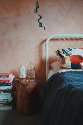 bedroom with coral pink limewash wall, navy blue duvet cover, stump side table and stack of books