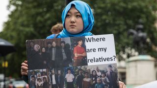 A photograph taken on August 5, 2021 in London, U.K. during a protest by the Uyghur Solidarity Campaign UK held outside the Chinese embassy. This image shows a member of the Uyghur community during a protest. The lady is wearing a light blue headscarf and is holding up a sign. The sign reads “Where are my relatives?” and includes several photos of the lady’s family.