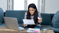 Worried woman holding credit card and calculating bills while sitting on the couch at home