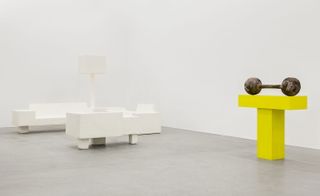 White models of a sofa, two chairs, a floor lamp and a yellow 'T' shape with a dumbbell on top of it.