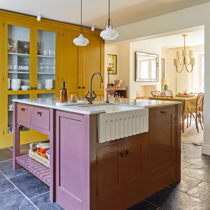 kitchen with yellow cabinetry and white range cooker style over, and plum-coloured island, look through to open plan dining area under an archway