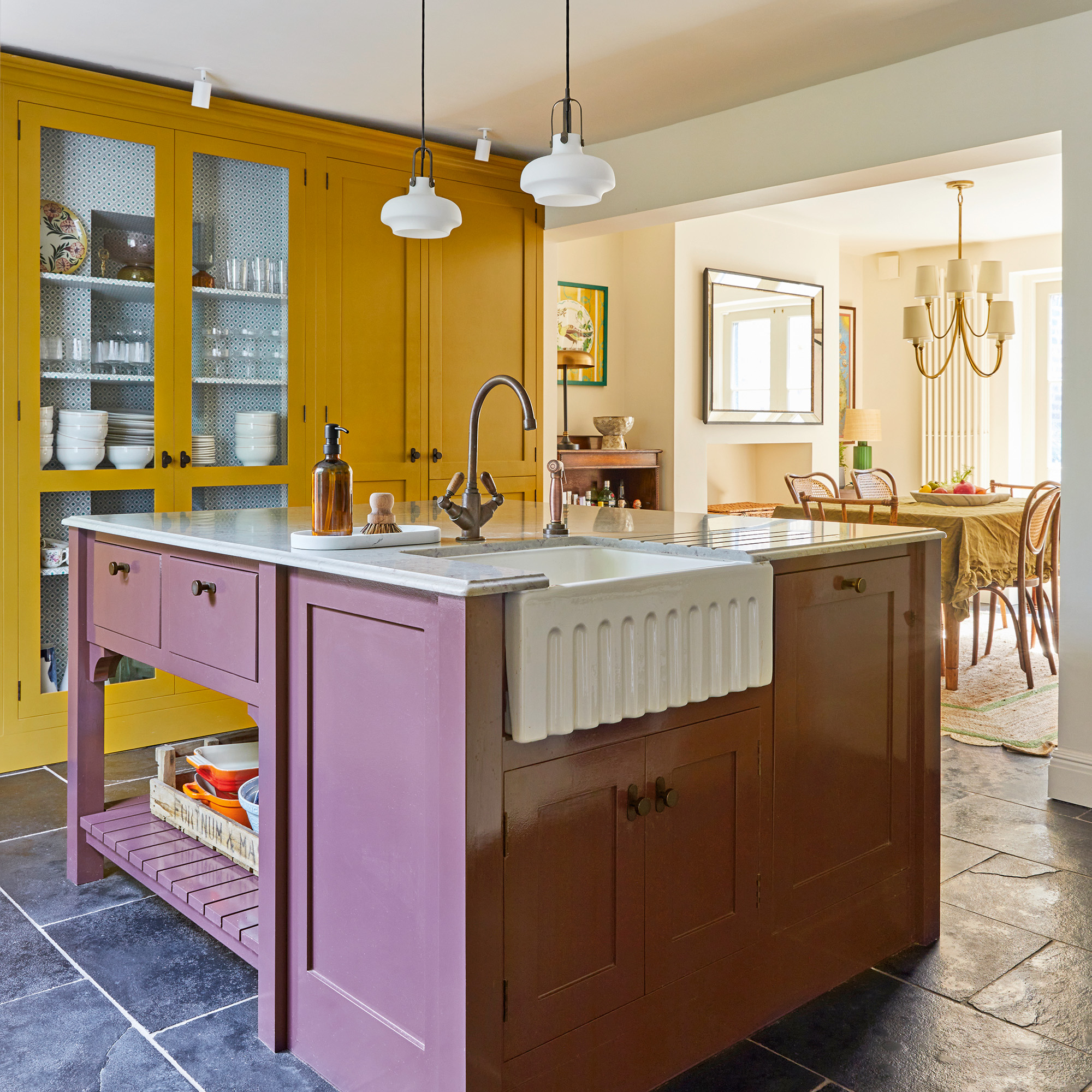 kitchen with yellow cabinetry and white range cooker style over, and plum-coloured island, look through to open plan dining area under an archway