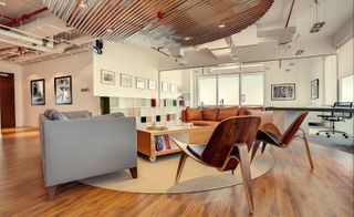 Office with grey and tan leather sofas, wooden chairs, wooden floor and wooden coffee table on castors
