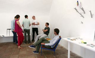 Designers in a room (some sitting and some standing) with items displayed on tables and walls