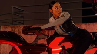 Greta Lee looking nervous and riding Red Tron Bike in Tron: Ares.