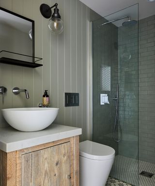 A small green bathroom with subway tiles in the shower and tongue and groove paneling on the walls