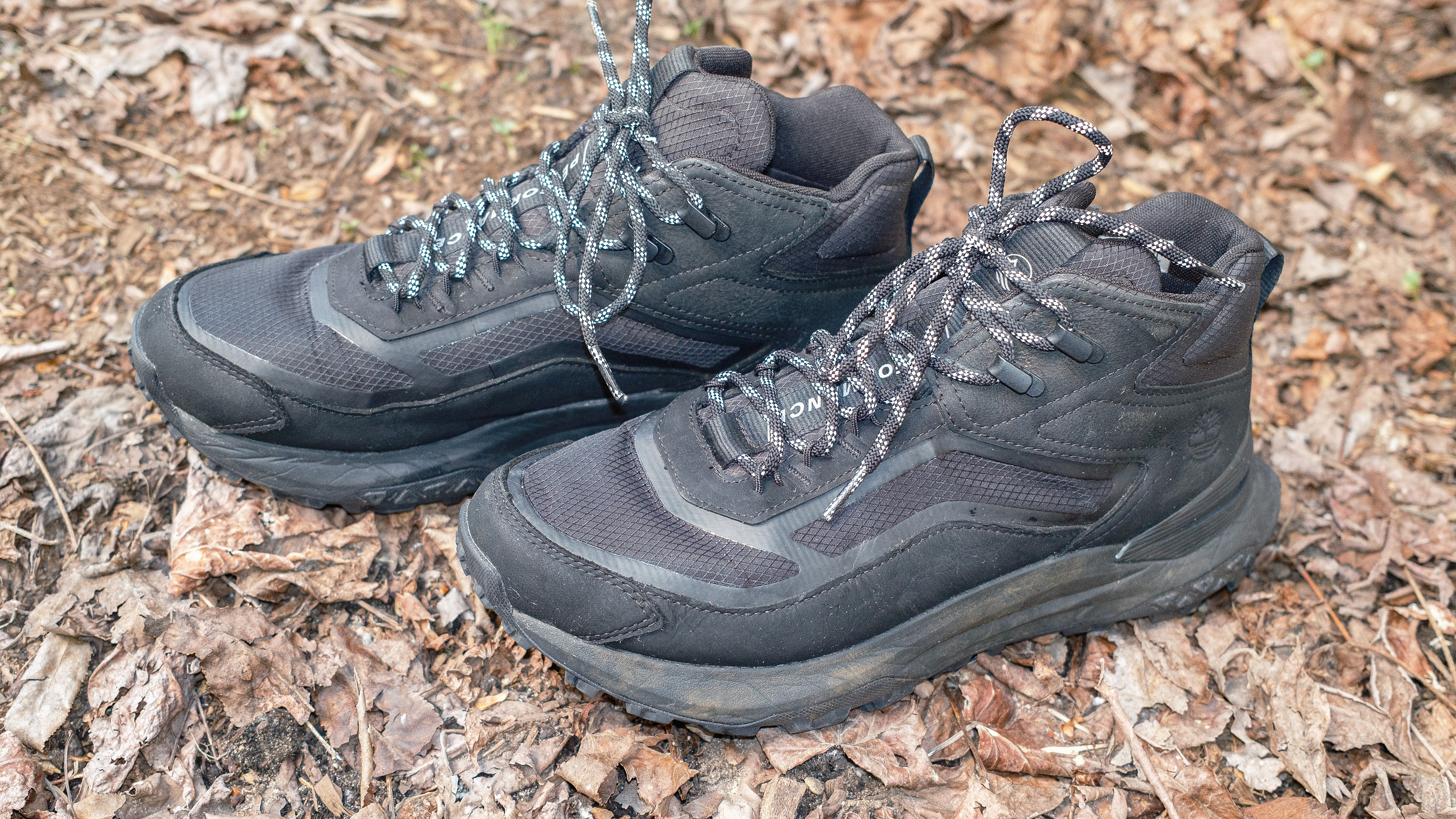 Close-up of a pair of Timberland Motion Access Mid Waterproof Sneakers (shown in black) sitting in leaves