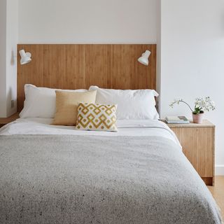Made up bed with white sheets and built in reading lights in wooden headboard