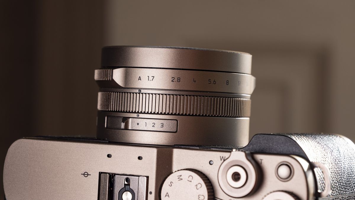Close up of the lens of the Titanium Gold special edition of the Panasonic Lumix L10 compact camera, on an antique wooden table