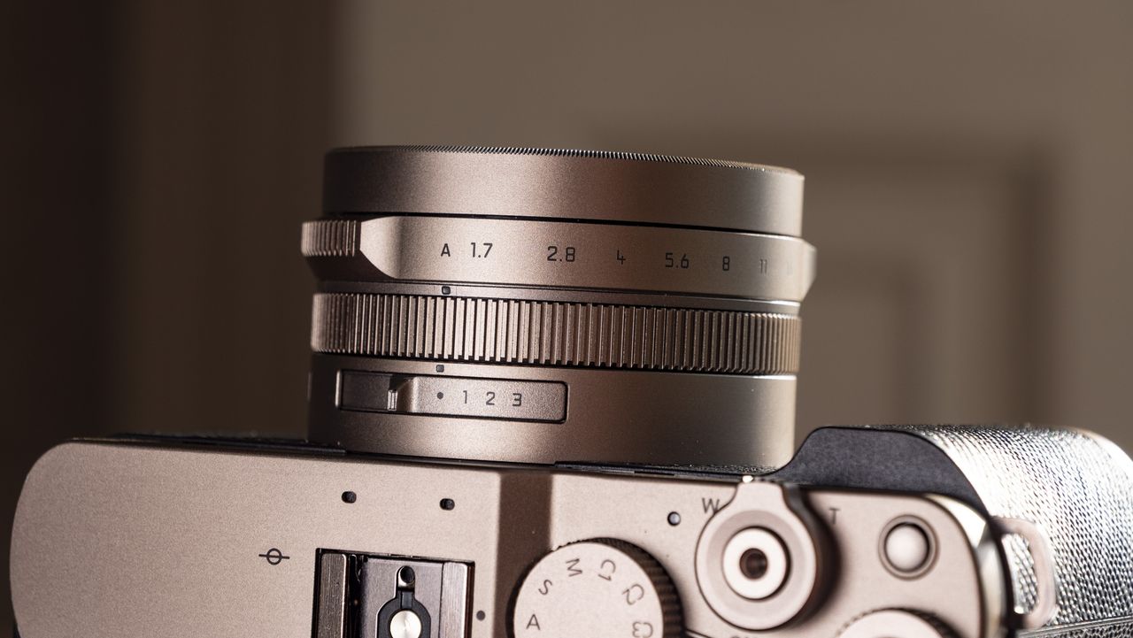 Close up of the lens of the Titanium Gold special edition of the Panasonic Lumix L10 compact camera, on an antique wooden table